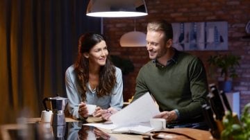 Two people reading the newspaper under a dim luminaire